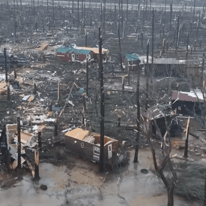 Overhead view of tornado damage in a residential area, with debris, fallen trees, and a destroyed shed filled with personal belongings.