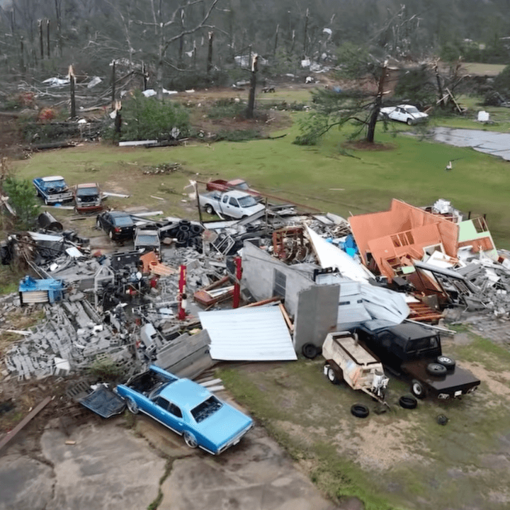 Aerial view of tornado destruction showing scattered debris, destroyed homes, and barren, broken trees in Mississippi.